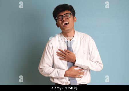 Indonesian senior high school student wearing white shirt uniform with gray tie laughing loudly while holding his chest. Fun comedy concept. Isolated Stock Photo