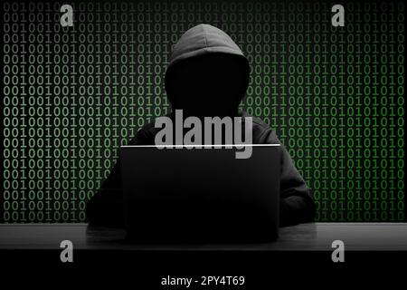 Mysterious man wearing black hoodie using laptop in the dark room. Hacker and cyber security concept. Stock Photo