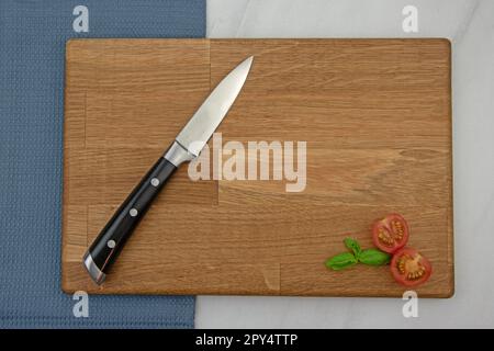 Tomato, basil and a knife on a wooden board with blue cloth Stock Photo