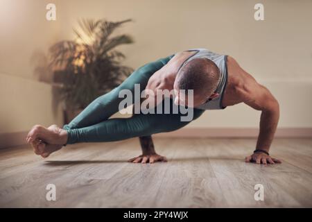 Yoga is a form of strength building. Full length shot of a handsome young man holding an eight angle pose during an indoor yoga session alone. Stock Photo