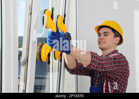 Worker using suction lifters during plastic window installation indoors Stock Photo