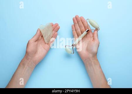 Woman holding gua sha tool and face roller on light blue background, top view Stock Photo
