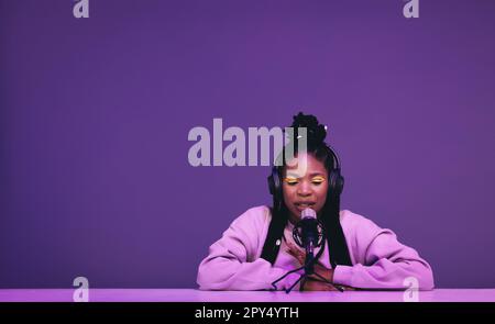 Female podcaster whispering into a microphone while hosting an asmr show. Woman recording a relaxing audio broadcast against a purple background. Blac Stock Photo