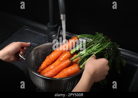 Woman washing fresh ripe juicy carrots under tap water in sink, closeup Stock Photo