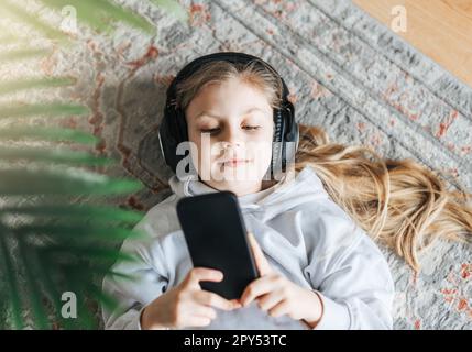 Smiling little girl listening music lying on the floor Stock Photo