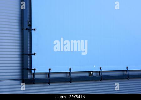Fragment of the outdoor light blue advertising banner fastened to the black metal frame with the help of plastic cable ties, mockup with copy space Stock Photo