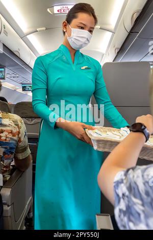 Vietnam Airlines cabin crew taking care of passengers, wearing ao dai uniform on flight from Bangkok to Vietnam Stock Photo