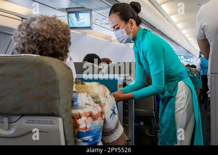 Vietnam Airlines cabin crew taking care of passengers, wearing ao dai uniform on flight from Bangkok to Vietnam Stock Photo
