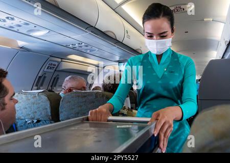 Vietnam Airlines cabin crew taking care of passengers, wearing ao dai uniform on flight from Bangkok to Vietnam Stock Photo