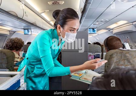 Vietnam Airlines cabin crew taking care of passengers, wearing ao dai uniform on flight from Bangkok to Vietnam Stock Photo