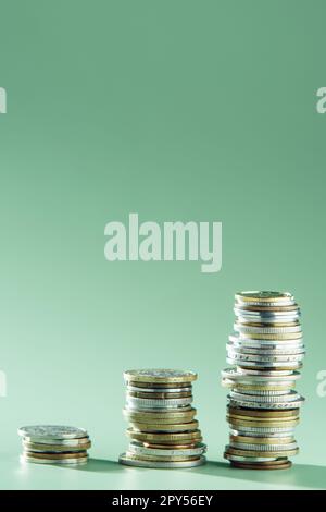 Side view of three stacks of different coins arranged in growing graph on green background. Money, business, investment. Stock Photo