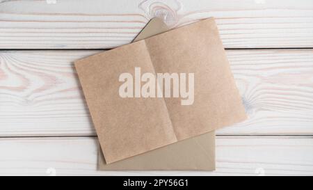 Top view of blank brown recycled craft paper on open craft envelope on grey wooden table. Correspondence, recycling. Stock Photo