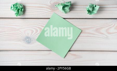 Flat lay of blank green sticker sticky note near crumpled notes on grey wooden table. Search, no idea, brainstorming. Stock Photo