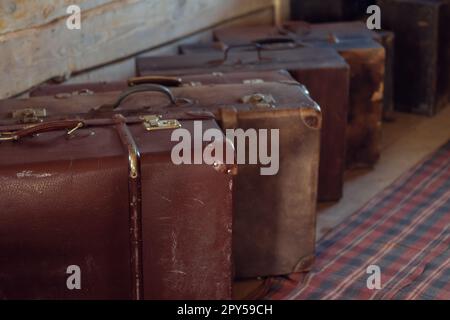 Row of antique shabby suitcases on floor of wooden countryside house. Brown leather old fashioned baggage for travelling Stock Photo