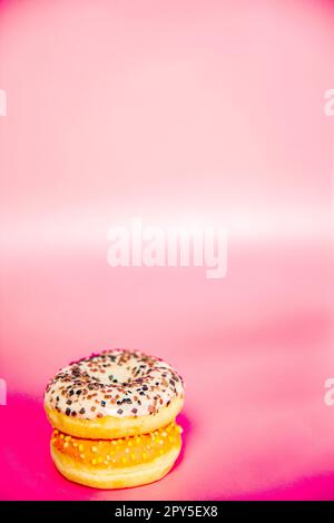 Sweet donuts stacked in a stack on a pink background. Copy space, various glaze and sprinkels chocolate chip, snack fast food sweets concept Stock Photo