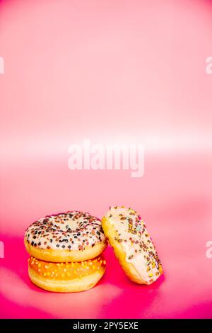 Sweet donuts stacked in a stack on a pink background. Copy space, various glaze and sprinkels chocolate chip, snack fast food sweets concept Stock Photo