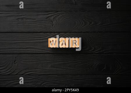 Wooden light yellow cubes with letters form the word War on a black wooden table. Flat lay, top view. Stock Photo