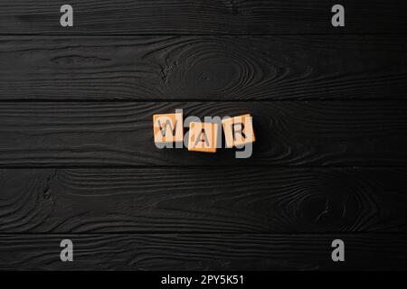 Wooden light yellow cubes with letters form the word War on a black wooden table. Flat lay, top view. Stock Photo