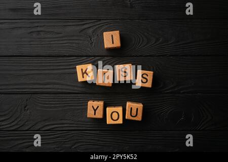 Wooden cubes with the phrase I Kiss You on a black background - a wooden table. Words of kiss are made of letters from wood for your girlfriend, boyfriend, wife, husband, for Valentine's Day greeting romantic postcard. Stock Photo