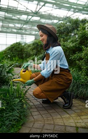 Young woman gardener with watering can caring for plants in hothouse Stock Photo