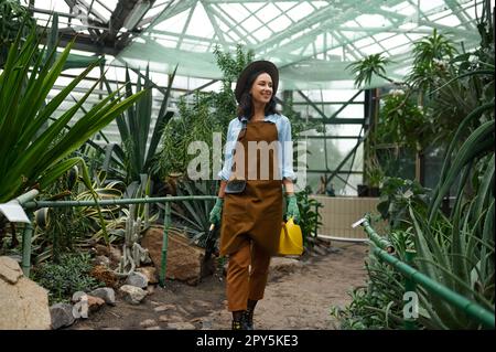 Young woman gardener in overalls leaving greenhouse after work Stock Photo