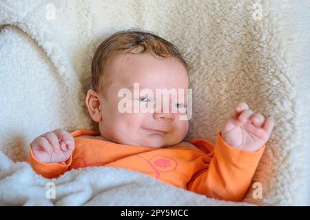 Kid in orange clothes raised his hand up while lying on a white blanket Stock Photo