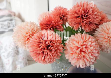 A bouquet of beautiful pink artificial flowers on a white table in the bedroom. Interior design. Romantic morning. Women's bedroom interior decoration. Bouquet in a vase. Stock Photo