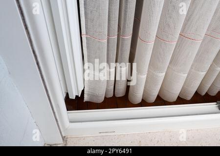 White coarse cotton or linen curtains made of weaves of thin threads. Simple compact economical apartment interior. Window decoration in the room. Red stripe. Stock Photo