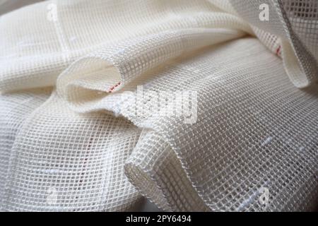White coarse cotton or linen curtains made of weaves of thin threads. Simple compact economical apartment interior. Window decoration in the room. Red stripe. Stock Photo