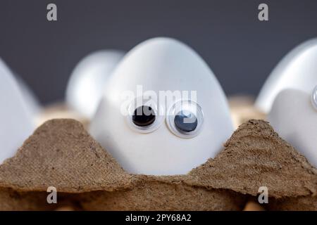 Funny faces on white eggs in carton box with organic chicken eggs on kitchen table closeup big animation eyes. humor, food and easter holiday concept. Stock Photo