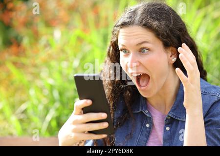 Amazed woman checking phone in a park Stock Photo