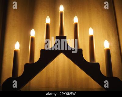 Schwibbogen arch luminaire in the form of a triangular candlestick. Yellow background. Evening, romantic, festive, religious or mystical atmosphere. Burning light bulbs that resemble candlelight Stock Photo