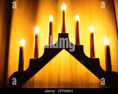 Schwibbogen arch luminaire in the form of a triangular candlestick. Yellow background. Evening, romantic, festive, religious or mystical atmosphere. Burning light bulbs that resemble candlelight Stock Photo