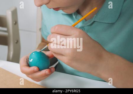Cropped portrait of boy hand, painting multi coloring Easter hens eggs, brown paper plate table, paintbrush Stock Photo