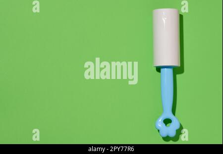 Roller with sticky tape for cleaning clothes on a green background, top view Stock Photo