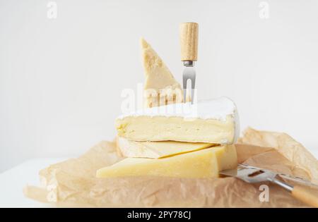 Different types of cheese lie on top of each other with cheese knives on parchment. A delicious delicacy. Stock Photo