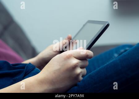 Cropped teenage boy hands holding digital tablet, watching movies or new, sitting on sofa. Streaming services online Stock Photo