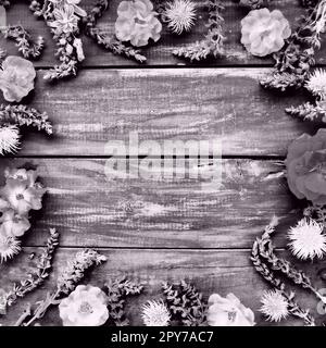 Flowers in a circle on a wooden background. Postcard roses, geraniums, lavender, sage and hairy chestnuts are placed along the edges. Background copy space, flat lay. Monochrome white - black photo. Stock Photo