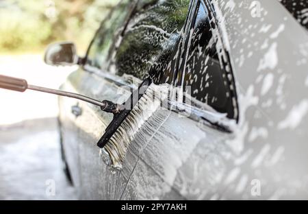 Side of silver car washed in self service manual carwash. Brush leaving strokes in white shampoo foam. Stock Photo