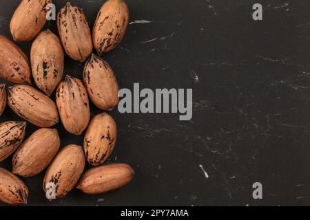 Tabletop view, whole pecan (Carya illinoinensis) nuts with spots on shells (Turkish variety) on black marble desk, space for text on right side. Stock Photo