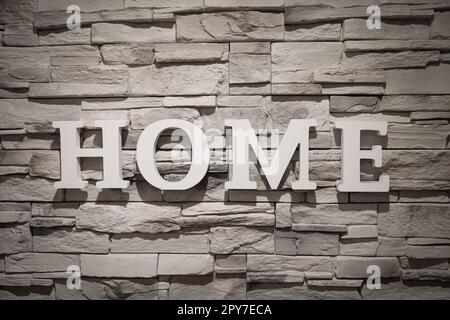 The word 'Home' is written on a wall covered with narrow stones. Stock Photo