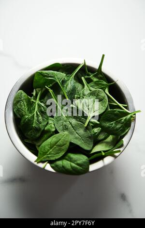 A bunch of Fresh baby spinach leaves in the in a stainless steel bowl on white marble background. Stock Photo