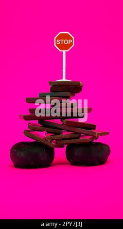 Chocolate and donuts on pink background with stop sign on top Stock Photo
