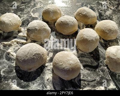 Round pieces of shortbread dough for making cookies or gingerbread. Raw buns or dumplings with scattered flour around on black background Stock Photo