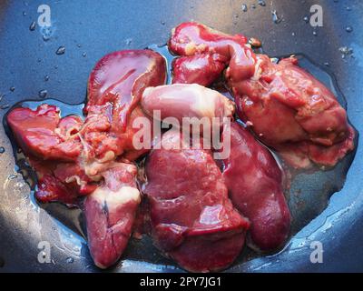 chicken liver, kidney and heart in a non-stick skillet. The offal of the bird is placed in a dark bowl and sprinkled with vegetable oil. Cooking food high in heme iron. Anti-anemic diet Stock Photo