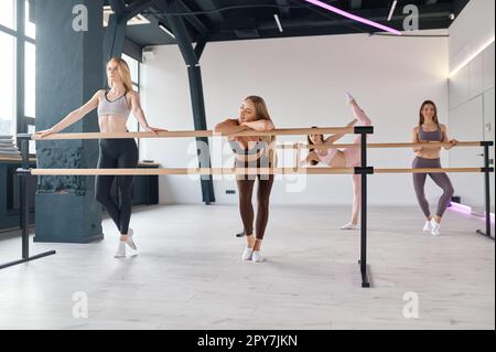 Young women dancers stretching legs, practicing ballet movement at barre Stock Photo