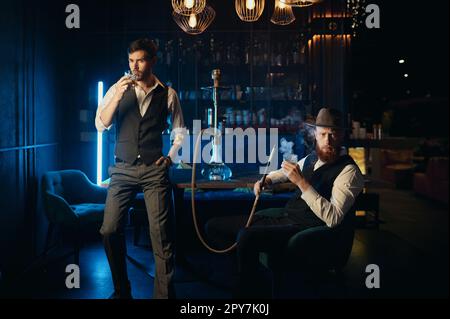 Serious guys smoking hookah while rest in pub Stock Photo