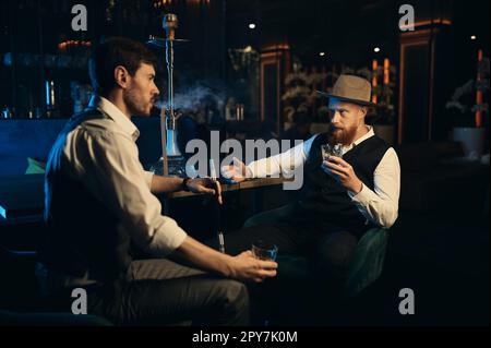 Guys having serious conversation while sitting face to face at hookah bar Stock Photo