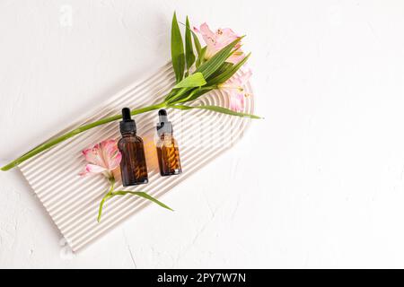 Two cosmetic bottles with a natural facial skin care product lie on a white plaster podium in the form of an arch with spring flowers. A copy space Stock Photo