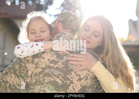 Daughter and wife hugging soldier in Ukrainian military uniform outdoors. Family reunion Stock Photo